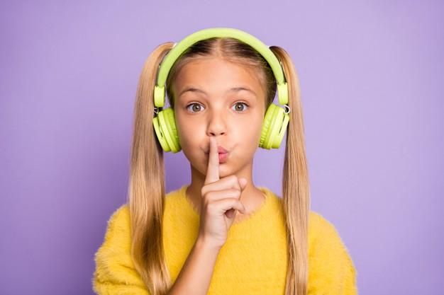Close up photo of astonished kid use headset listen music find melody in playlist show index finger dont tell confidential information wear pullover isolated purple color wall Premium Photo